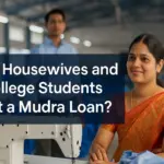 A smiling Indian housewife in a traditional saree sitting confidently beside a sewing machine in a small garment workshop, with a male figure blurred in the background. The overlaid text reads “Can Housewives and College Students Get a Mudra Loan?” in bold, white sans-serif font on a semi-transparent blue box.