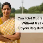 An Indian woman in a yellow and white sari stands confidently outside a small industrial unit, with a clean semi-transparent text box beside her reading “Can I Get Mudra Loan Without GST or Udyam Registration?” The background features a blue-roofed warehouse, gravel, and greenery, symbolizing micro-enterprise in a rural or semi-urban setting.