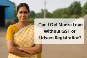 An Indian woman in a yellow and white sari stands confidently outside a small industrial unit, with a clean semi-transparent text box beside her reading “Can I Get Mudra Loan Without GST or Udyam Registration?” The background features a blue-roofed warehouse, gravel, and greenery, symbolizing micro-enterprise in a rural or semi-urban setting.
