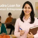 A professional image showing confident Indian women entrepreneurs in a workspace. One woman is holding a notebook and pen, others are working on a sewing machine and computer, with a map of India in the background. Text reads “Mudra Loan for Women Entrepreneurs” with the Mudra logo, designed cleanly with Indian elements and proper padding.