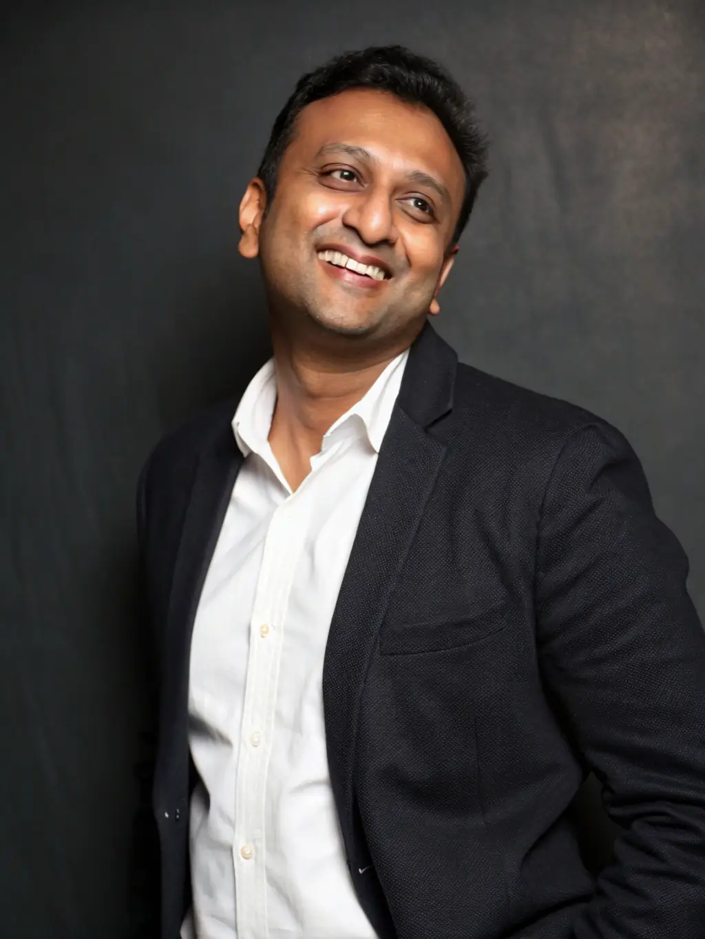 A professional headshot of CA Manish Gugliya, a Chartered Accountant with 20+ years of experience, smiling confidently and looking directly at the camera. The background is a blurred office setting.